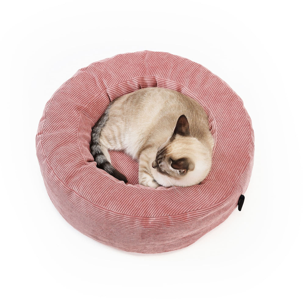 Lit pour chat NEST en rose, un chat siamois dormant roulé en boule dans le lit rond en velours côtelé