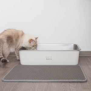 katze in weißem katzenklo und davor liegt die katzenstreu matte in grau