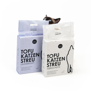 Zwei Beutel Tofu Katzenstreu nebeneinander, zwei Varianten: Geruchlos und Lavendel, Katze schaut von hinten darüber